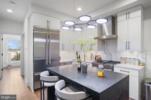 kitchen featuring light wood finished floors, white cabinets, high quality appliances, wall chimney range hood, and backsplash