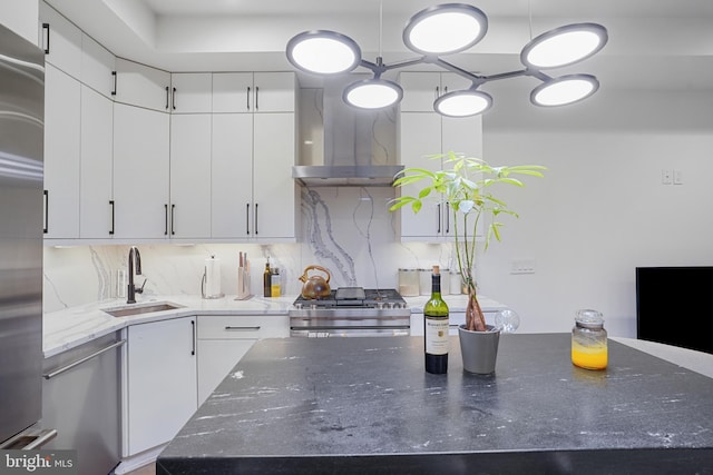 kitchen with stainless steel appliances, decorative backsplash, white cabinetry, a sink, and wall chimney exhaust hood