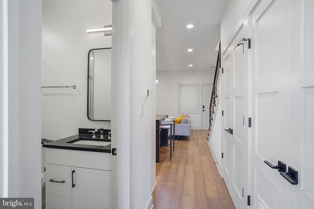 hall featuring light wood-style floors, recessed lighting, and a sink