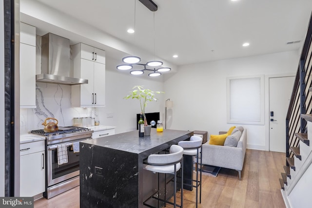 kitchen featuring a breakfast bar, light wood-style flooring, decorative backsplash, stainless steel gas stove, and wall chimney exhaust hood