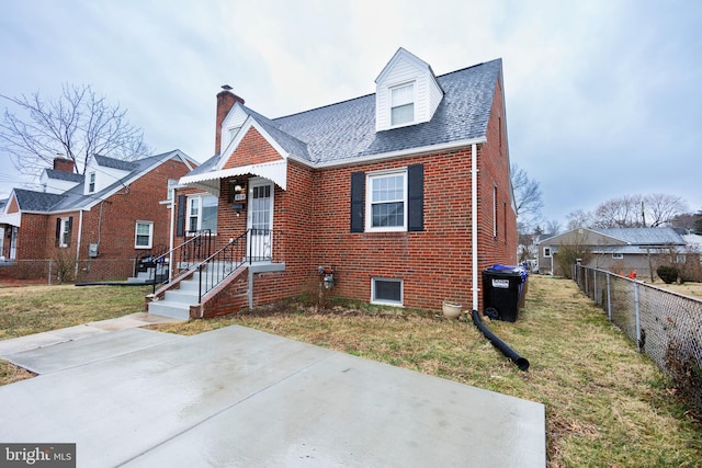 view of front of property with a shingled roof, fence, a front lawn, and brick siding