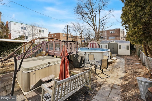 view of patio featuring an outbuilding, fence, grilling area, a storage unit, and a hot tub