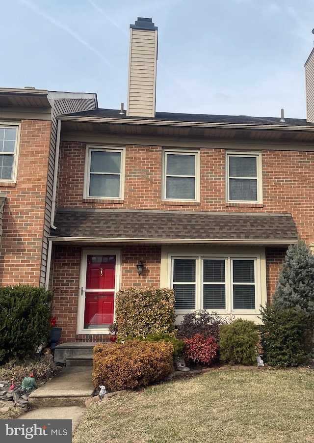 multi unit property featuring a shingled roof, brick siding, and a chimney