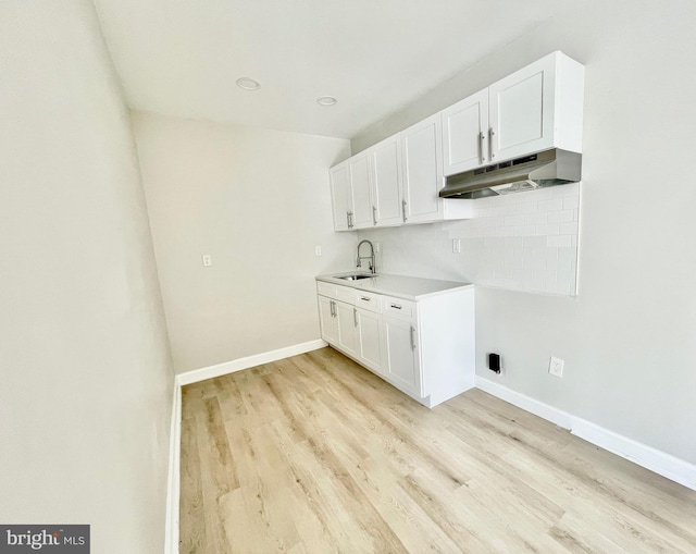 kitchen with under cabinet range hood, a sink, white cabinets, decorative backsplash, and light wood finished floors