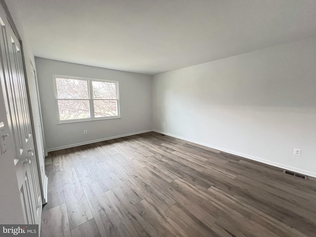 spare room featuring dark wood-type flooring, visible vents, and baseboards