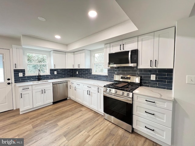 kitchen featuring tasteful backsplash, appliances with stainless steel finishes, light wood-style floors, white cabinets, and a sink