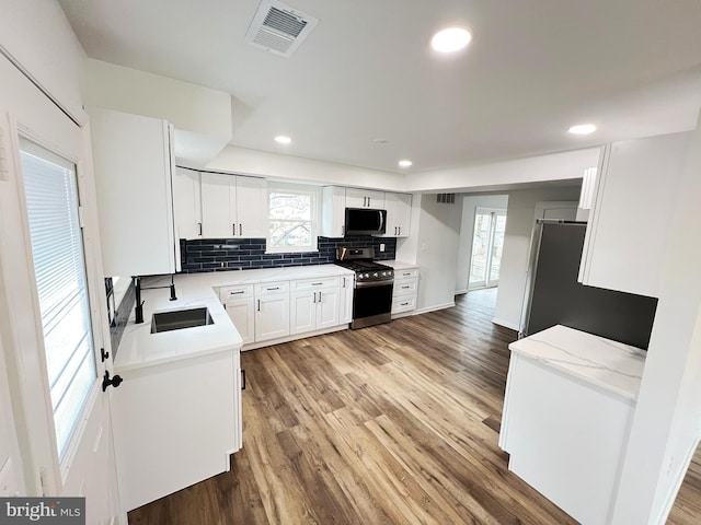 kitchen with stainless steel appliances, visible vents, backsplash, light wood-style flooring, and a sink