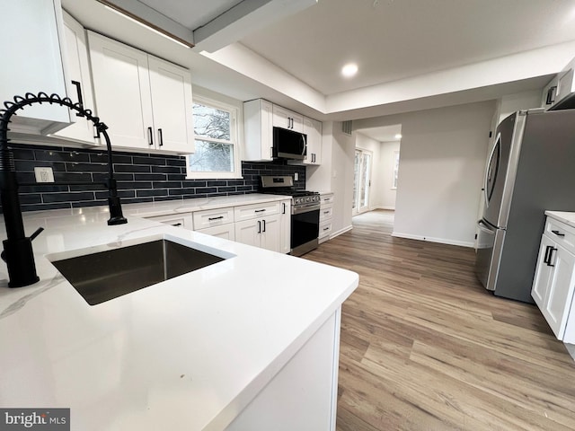 kitchen featuring light wood finished floors, appliances with stainless steel finishes, white cabinets, and decorative backsplash