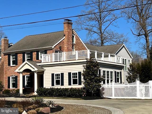 view of front facade with driveway, brick siding, fence, and a chimney