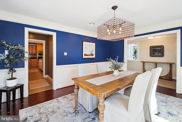 dining room featuring a wainscoted wall, ornamental molding, wood finished floors, and an inviting chandelier