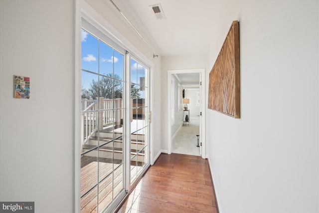 hallway with hardwood / wood-style flooring, baseboards, and visible vents