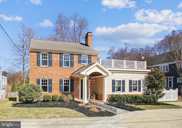 view of front of home featuring brick siding, a chimney, a front lawn, and a balcony