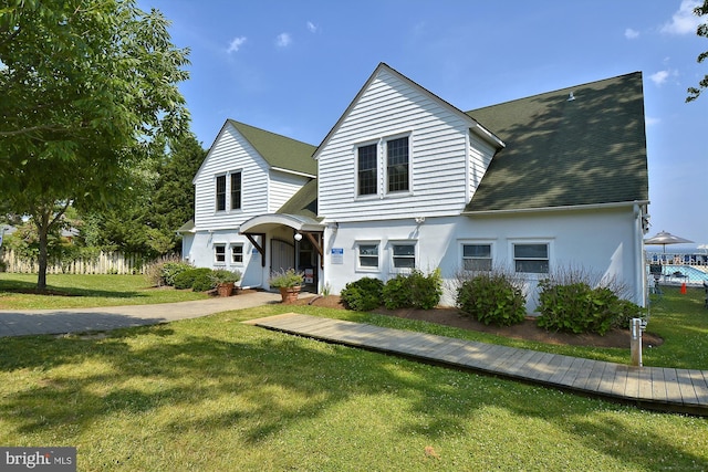 view of front of house featuring a front lawn, roof with shingles, fence, and stucco siding