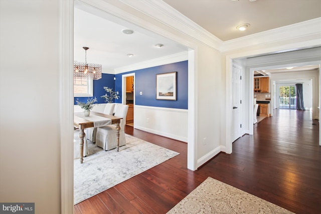 corridor with baseboards, wainscoting, dark wood-style flooring, crown molding, and a notable chandelier