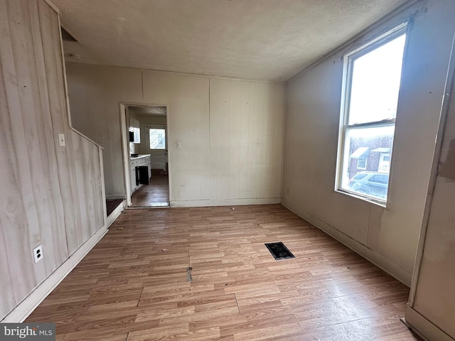 spare room featuring light wood-style floors, a wealth of natural light, and visible vents