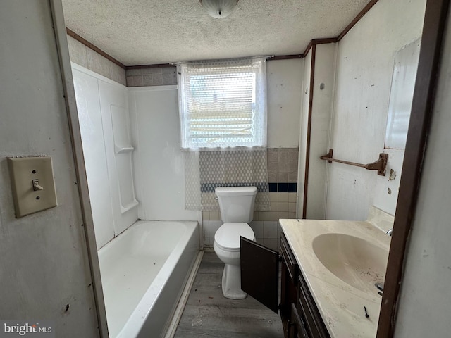 bathroom with a tub to relax in, toilet, a textured ceiling, vanity, and wood finished floors