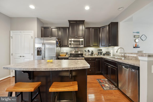 kitchen with stainless steel appliances, light countertops, light wood-style floors, a kitchen bar, and a sink