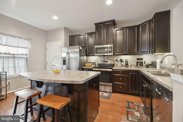 kitchen with a center island, stainless steel appliances, light countertops, light wood-style floors, and a sink