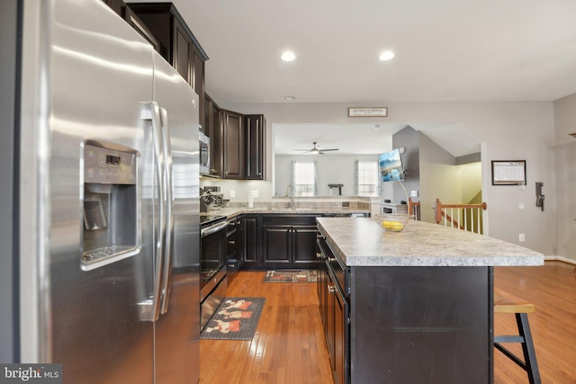 kitchen with a kitchen island, appliances with stainless steel finishes, wood finished floors, a kitchen bar, and a sink