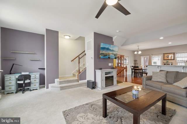 living area featuring baseboards, visible vents, a ceiling fan, stairs, and carpet flooring