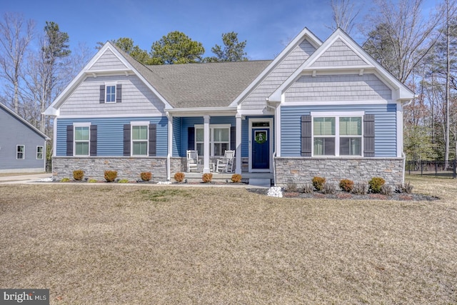 craftsman-style house with a front yard, stone siding, covered porch, and fence