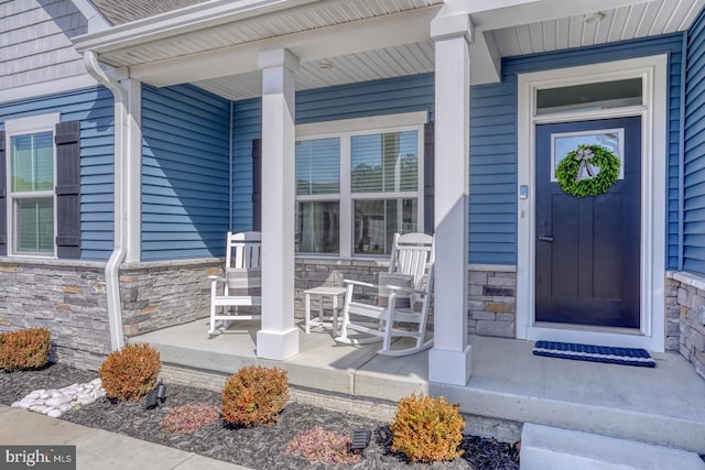 view of exterior entry with stone siding and covered porch