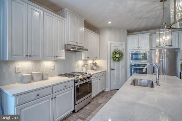 kitchen with under cabinet range hood, white cabinetry, appliances with stainless steel finishes, and a sink