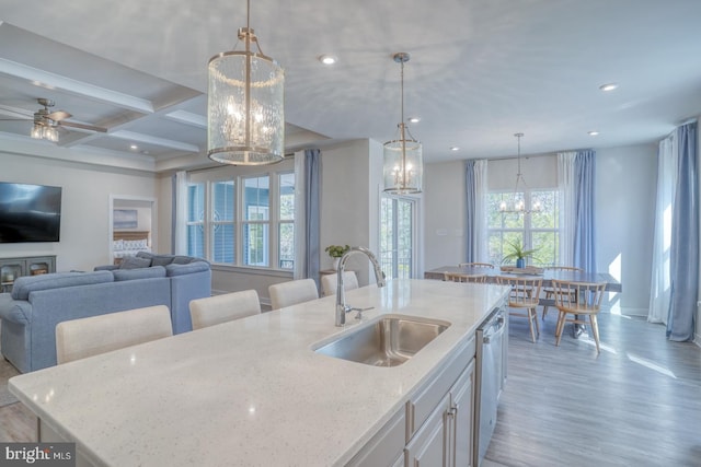 kitchen with coffered ceiling, a sink, light stone countertops, dishwasher, and light wood finished floors