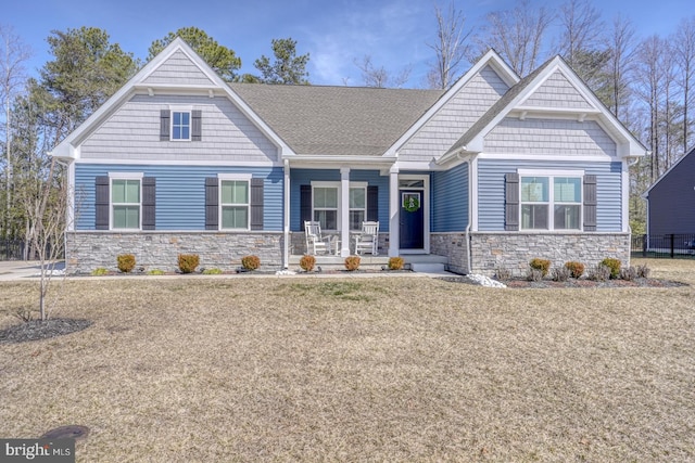 craftsman inspired home with stone siding, a porch, and a front lawn