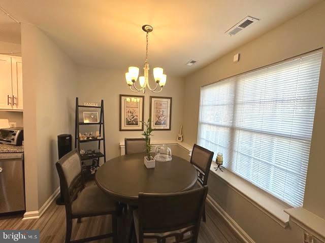 dining area featuring baseboards, visible vents, a chandelier, and wood finished floors