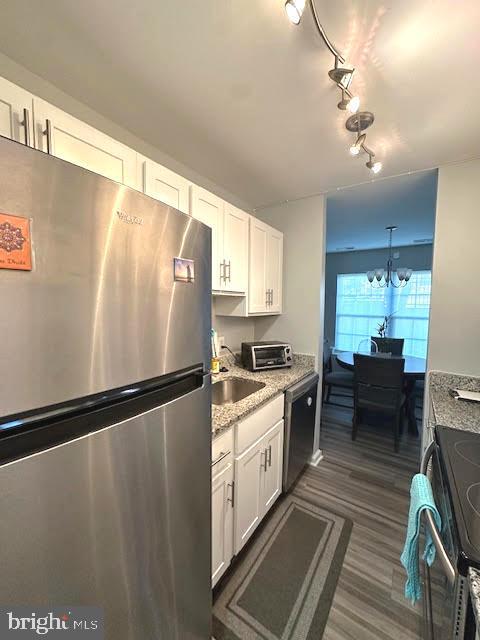 kitchen featuring a notable chandelier, stainless steel appliances, dark wood-type flooring, white cabinets, and a sink