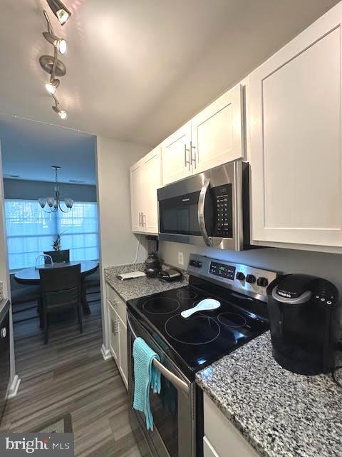 kitchen with stone counters, stainless steel appliances, dark wood-type flooring, white cabinetry, and an inviting chandelier