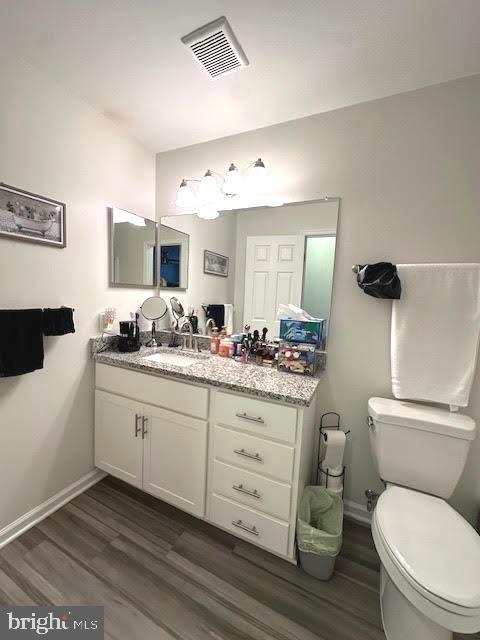 bathroom featuring toilet, wood finished floors, visible vents, and baseboards