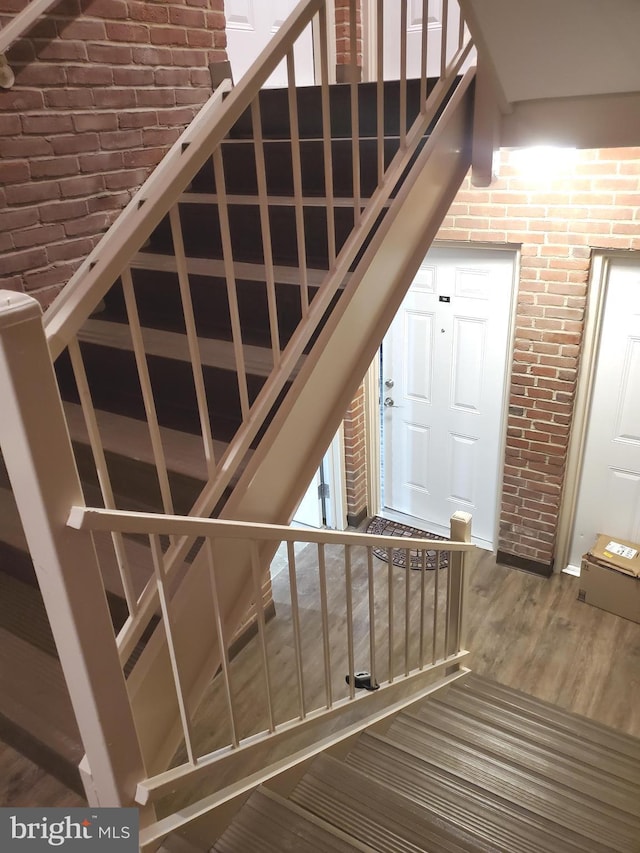 stairs with brick wall and wood finished floors