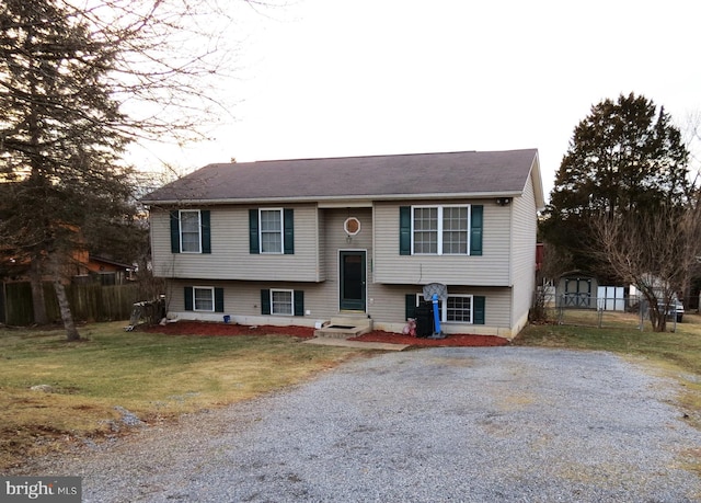 raised ranch featuring entry steps, fence, driveway, and a front lawn