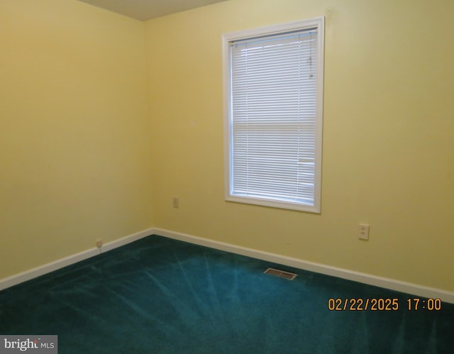 spare room with dark carpet, visible vents, and baseboards