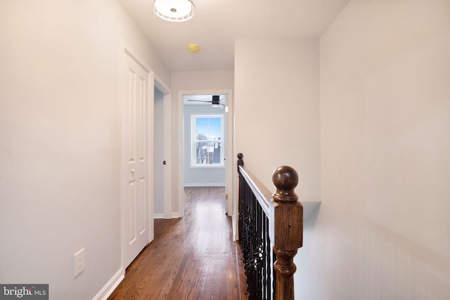 hallway with baseboards, wood finished floors, and an upstairs landing