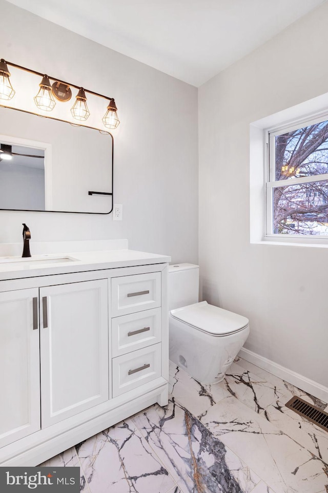 half bath with toilet, visible vents, vanity, baseboards, and marble finish floor