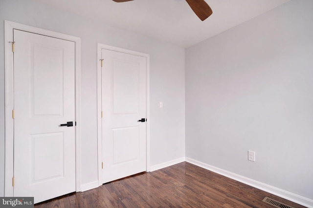 unfurnished bedroom featuring dark wood-style floors, visible vents, baseboards, and ceiling fan