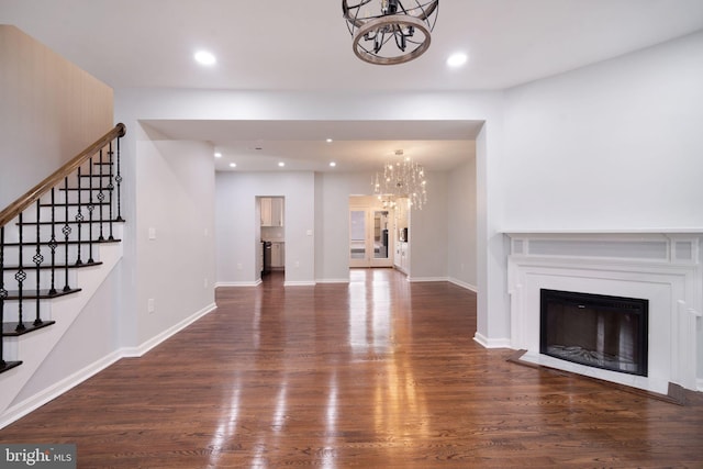 unfurnished living room with a glass covered fireplace, wood finished floors, stairs, a chandelier, and recessed lighting