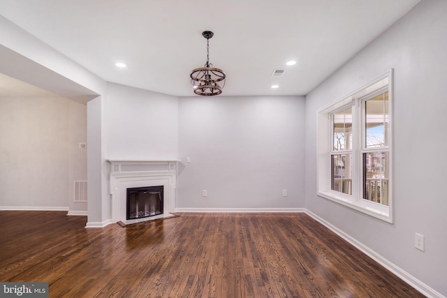 unfurnished living room with baseboards, visible vents, a fireplace with raised hearth, and dark wood finished floors