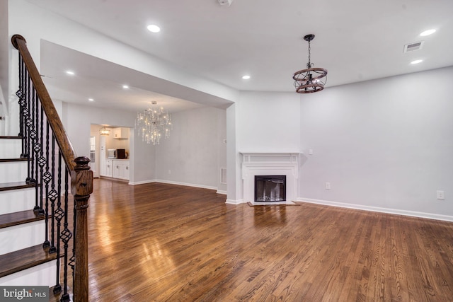 unfurnished living room with a fireplace, a notable chandelier, visible vents, stairway, and wood finished floors