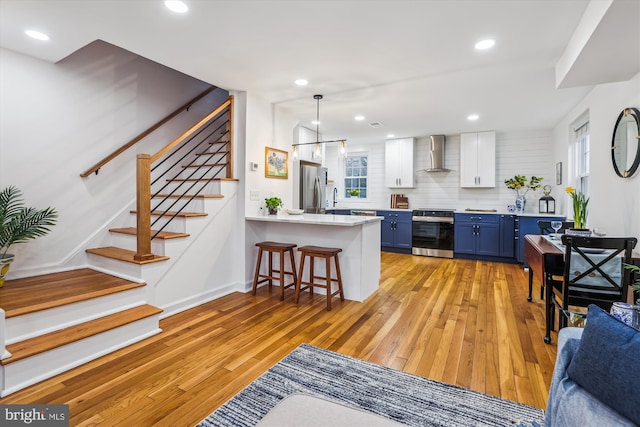 kitchen featuring a breakfast bar area, appliances with stainless steel finishes, blue cabinets, a peninsula, and wall chimney exhaust hood