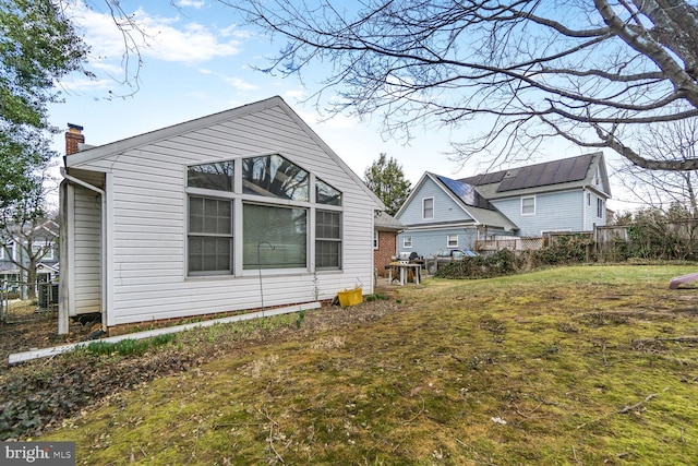 rear view of property with a lawn, a chimney, and fence