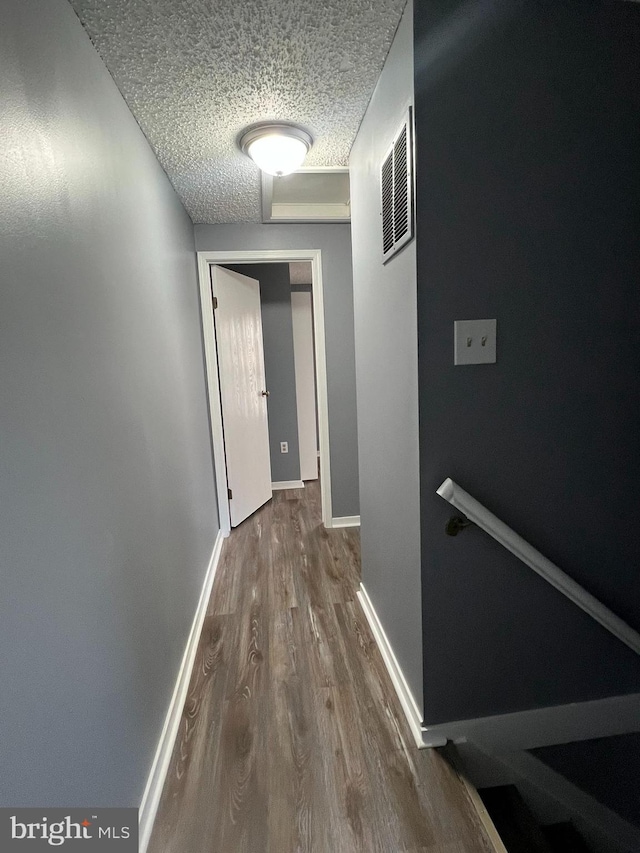 corridor with dark wood-style flooring, visible vents, a textured ceiling, and baseboards