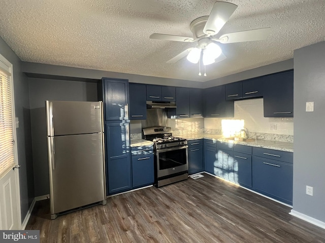 kitchen featuring under cabinet range hood, a sink, appliances with stainless steel finishes, blue cabinetry, and dark wood-style floors