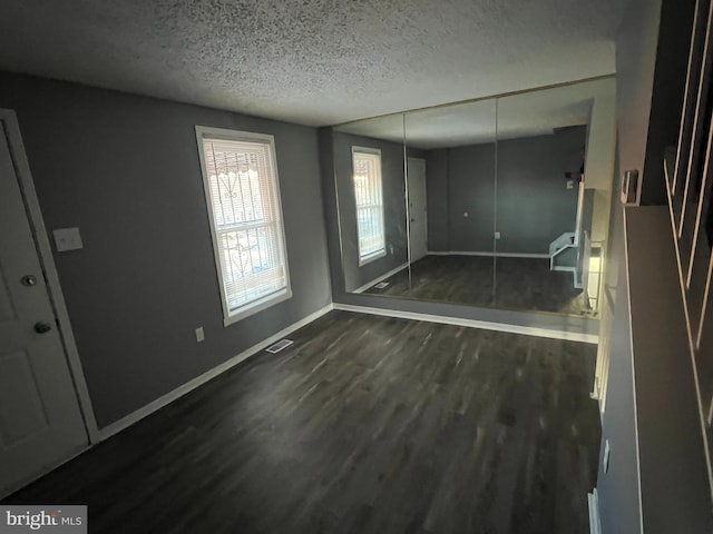 interior space with dark wood-style floors, visible vents, a textured ceiling, and baseboards