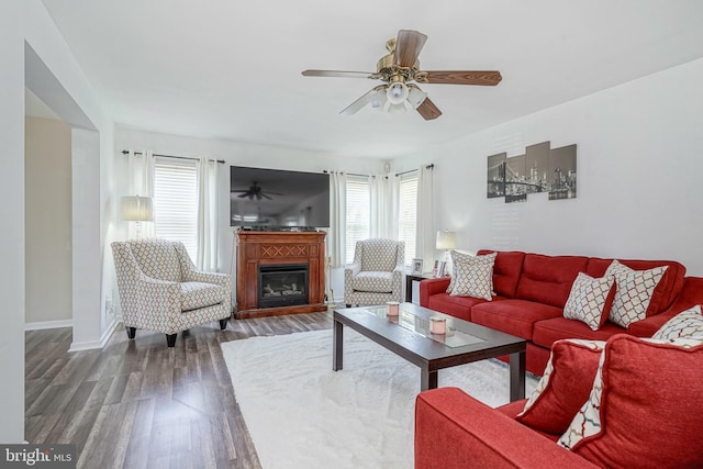 living area with a glass covered fireplace, wood finished floors, a ceiling fan, and baseboards