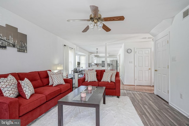 living area with visible vents, light wood-type flooring, a ceiling fan, and baseboards