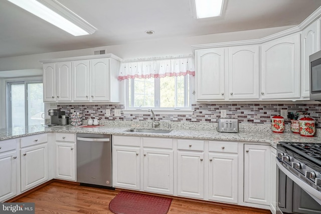 kitchen with wood finished floors, appliances with stainless steel finishes, a sink, and white cabinets